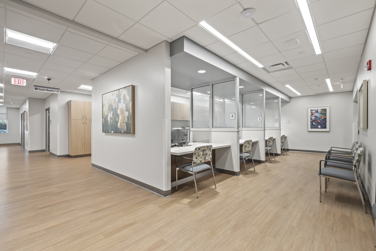 Next to a reception area, the hall of the cancer center has signage directing patients to Exam Rooms 1-8.