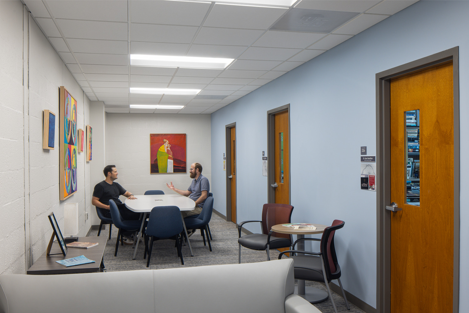 Two men sit and talk in a common area in Bowman Hall decorated with colorful artwork and a pastel blue accent wall.