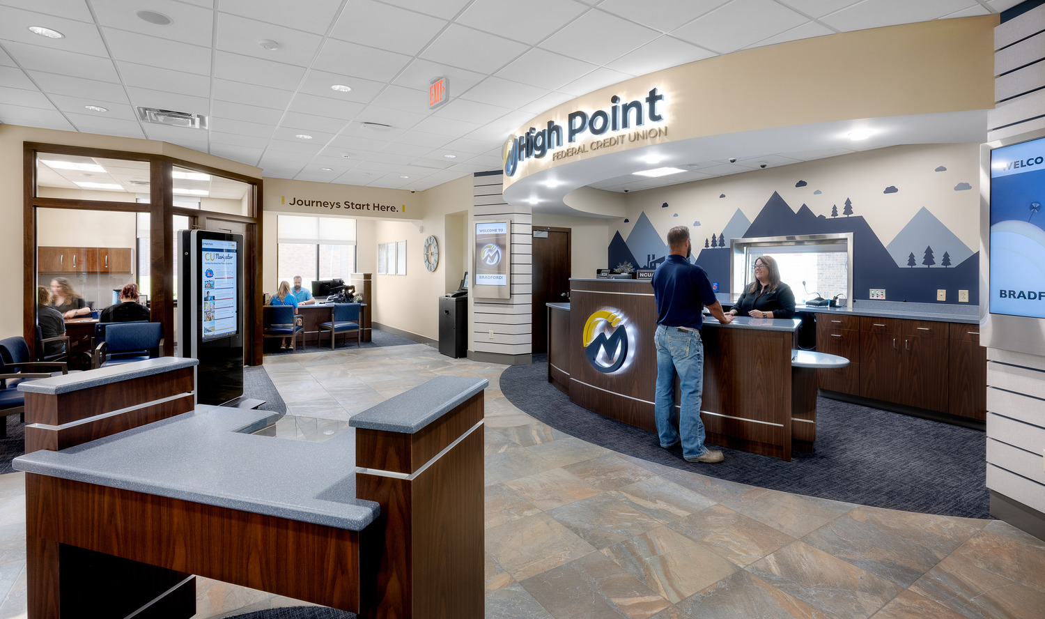 The High Point Federal Credit Union Bradford Branch's spacious lobby, a rounded reception desk, various employees meeting with clients, signage, a waiting area, and information kiosks.