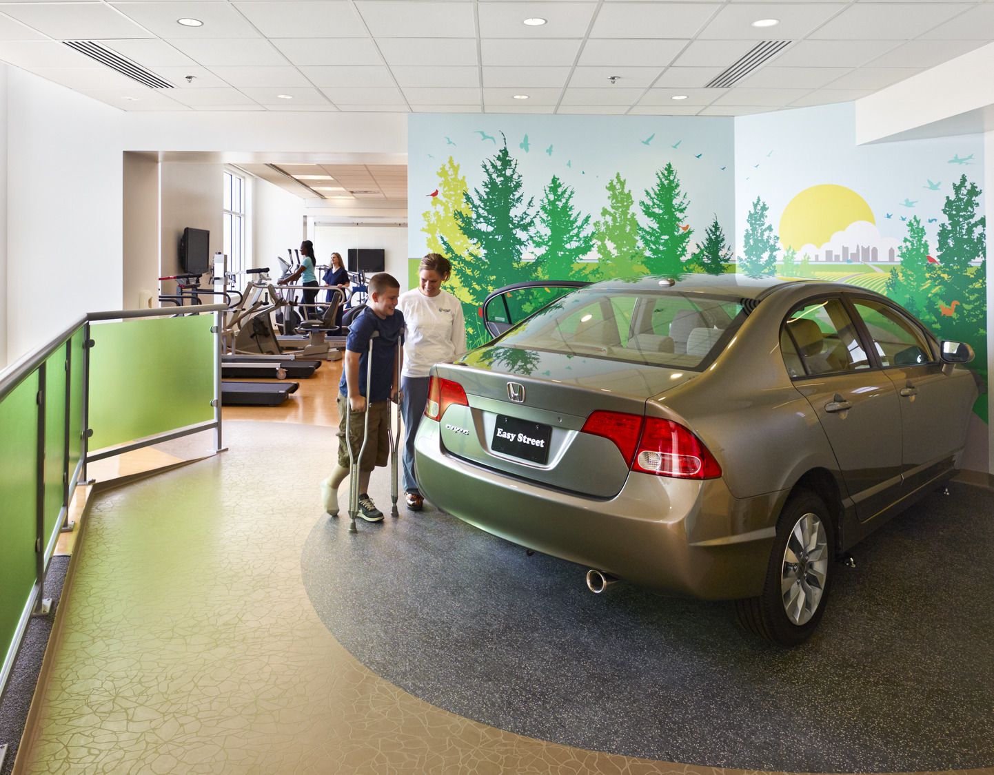 Adjacent to a fitness center, a boy on crutches smiles at an interactive car display in front of a colorful mural at Nationwide Children's Hospital