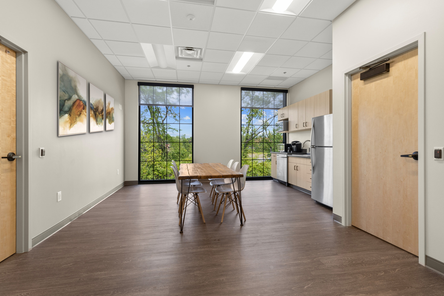 A brightly lit breakroom at Vive Vascular with a table and chairs, counter with kitchen appliances, cabinets, abstract wall art and tall windows.