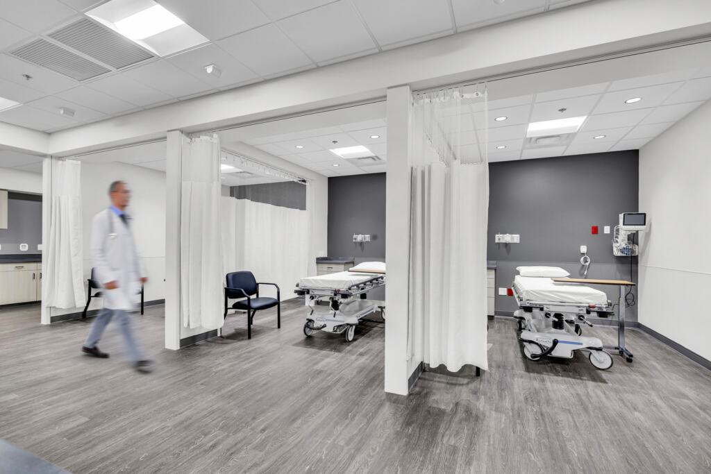 A doctor walks past three side-by-side patient bays in Trillium Surgery Center.