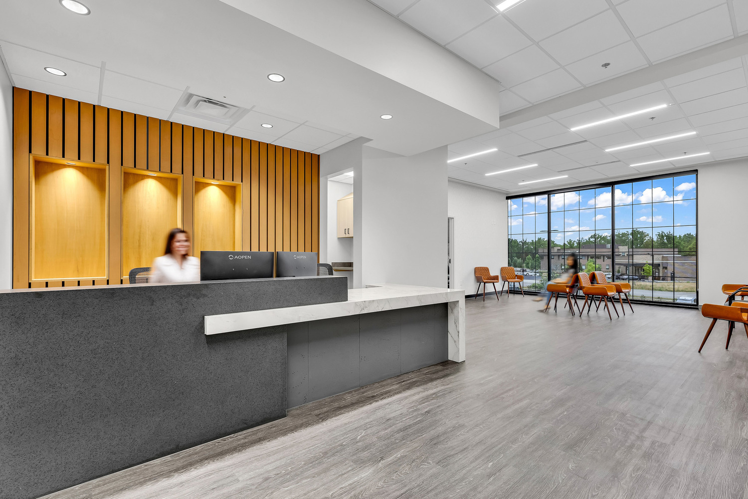 A warm and inviting reception and waiting area with wooden details, orange chairs and floor-to-ceiling windows.