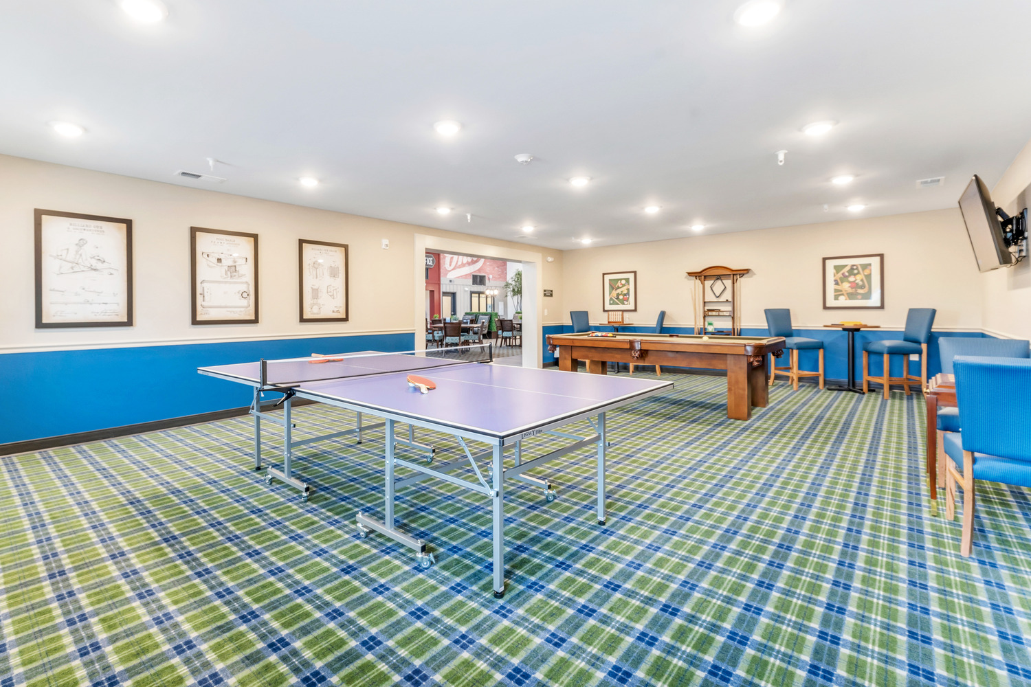 A recreation room in Homestead Village Active Senior Living Facility with bright green and blue tartan carpeting, pool table, and table tennis.