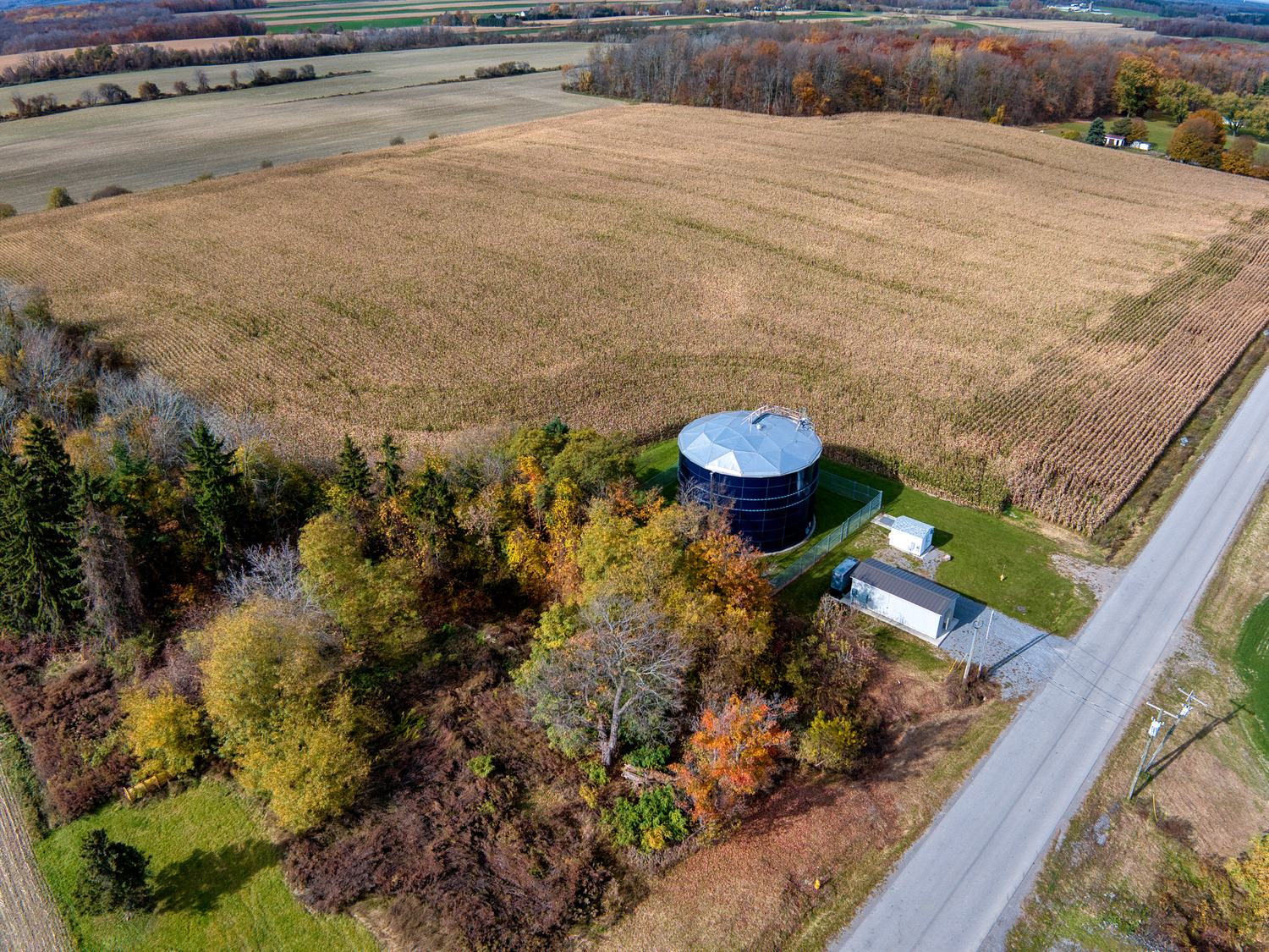 Aerial view of a large circular silo in the Town of York beside a road, surrounded by vibrant autumn trees and vast farmland. The scene conveys a tranquil, rural atmosphere.