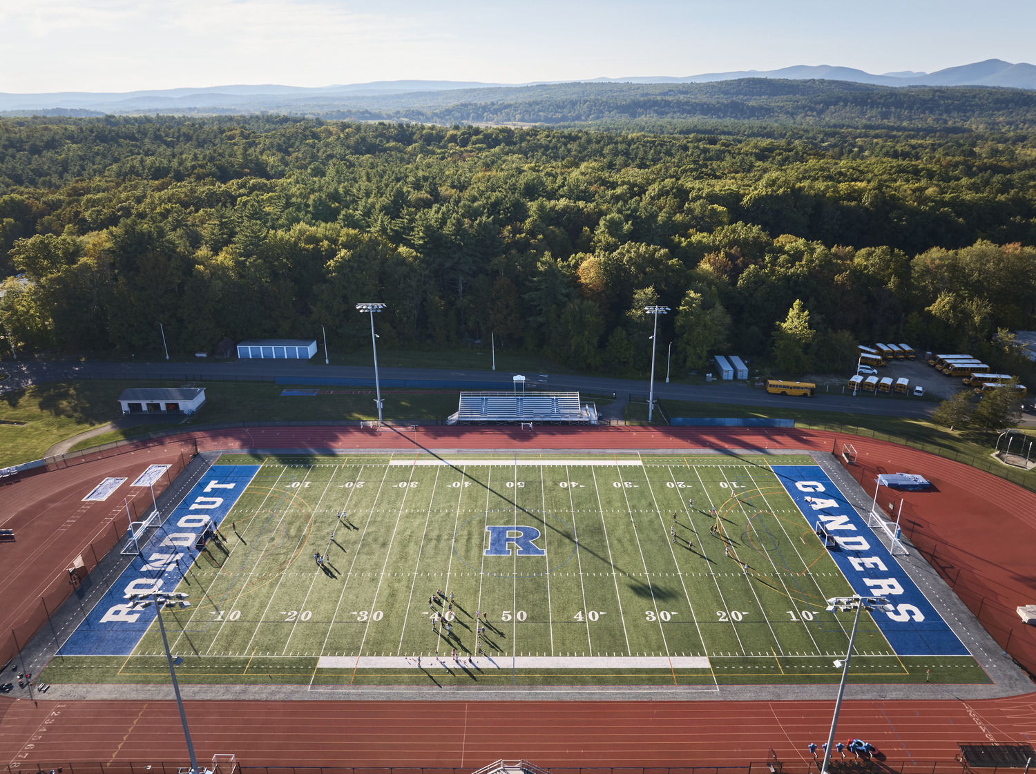 Rondout Valley CSD – 2019 Bond Referendum An aerial view of the Rondout Valley CSD Athletic Complex renovation, including a renovated field, track, and stands, against a forest backdrop.