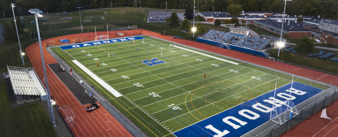 The Rondout Valley CSD K-12 Athletic Complex renovation with synthetic turf and LED lighting at night, illuminated by stadium lights, on the academic campus.