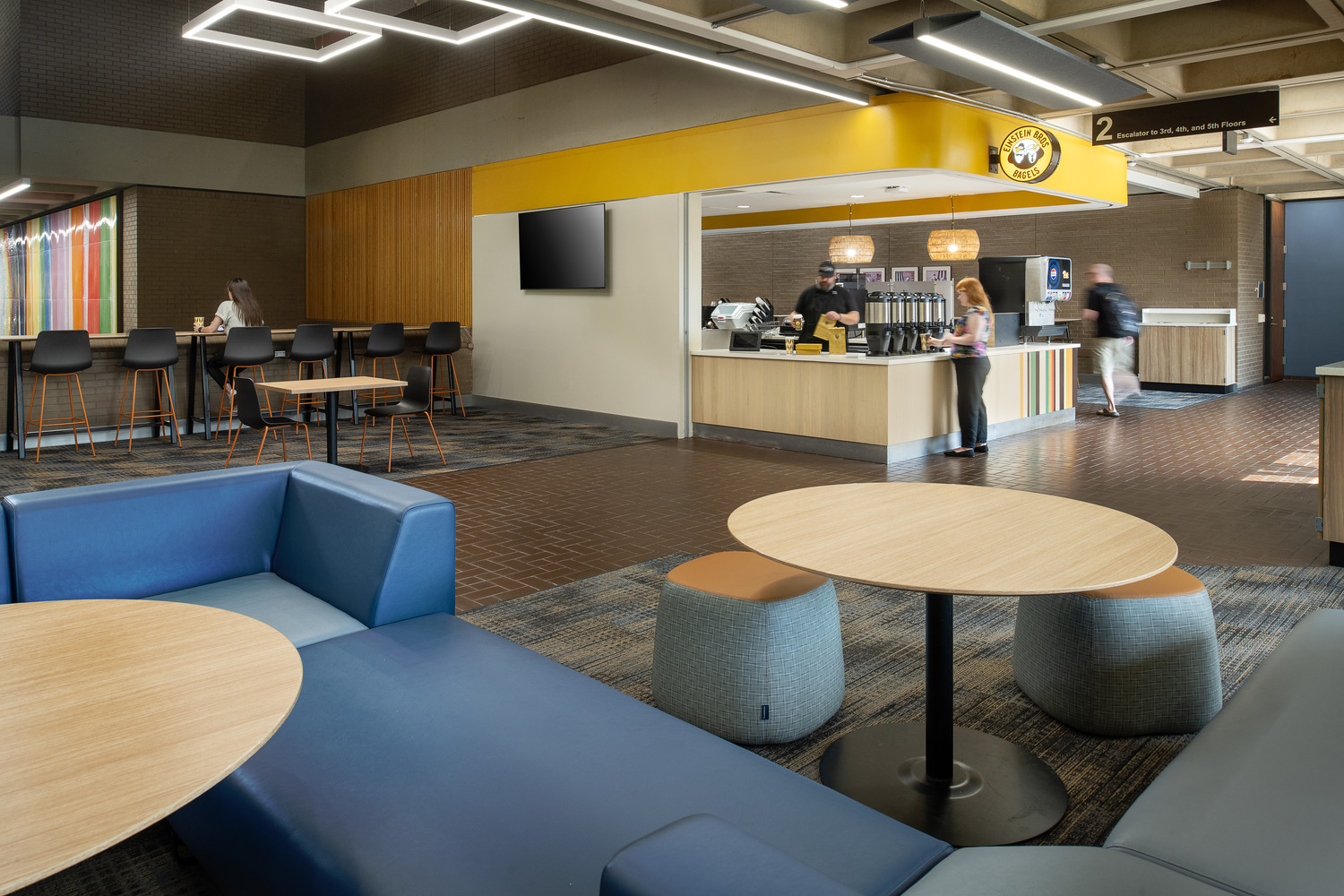 University of Pittsburgh – Einstein Bros Bagels Renovations at Posvar Hall A student pours coffee at Einstein Bros Bagels, a rectangular counter space below a bright yellow drop ceiling.