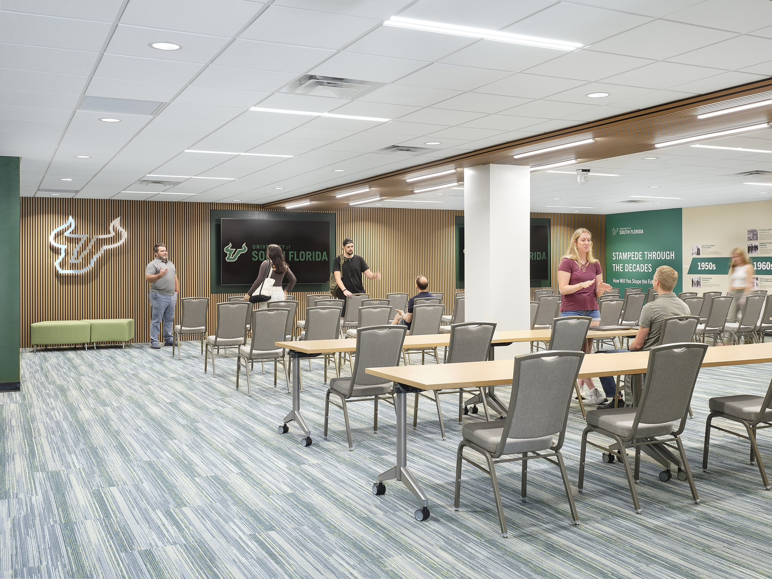 University of South Florida – Campus Visitation Center Rows of chairs at long tables face a screen at the head of a well-lit gathering space inside the visitation center.