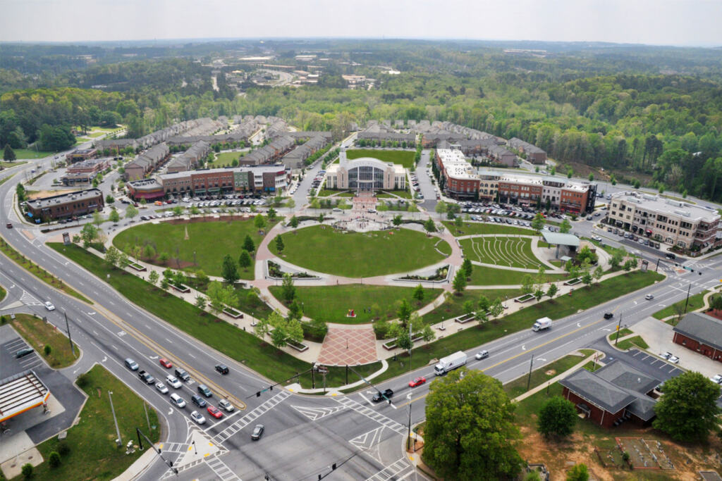 Aerial view of Suwanee Town Center with a circular green park surrounded by roads and buildings. Streets are busy with cars, trees dot the landscape.
