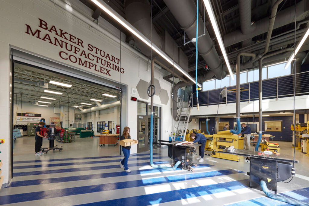 A modern workshop with high ceilings and industrial lighting in the Baker Stuart Manufacturing Complex. Several people work on projects, creating a busy and productive atmosphere.