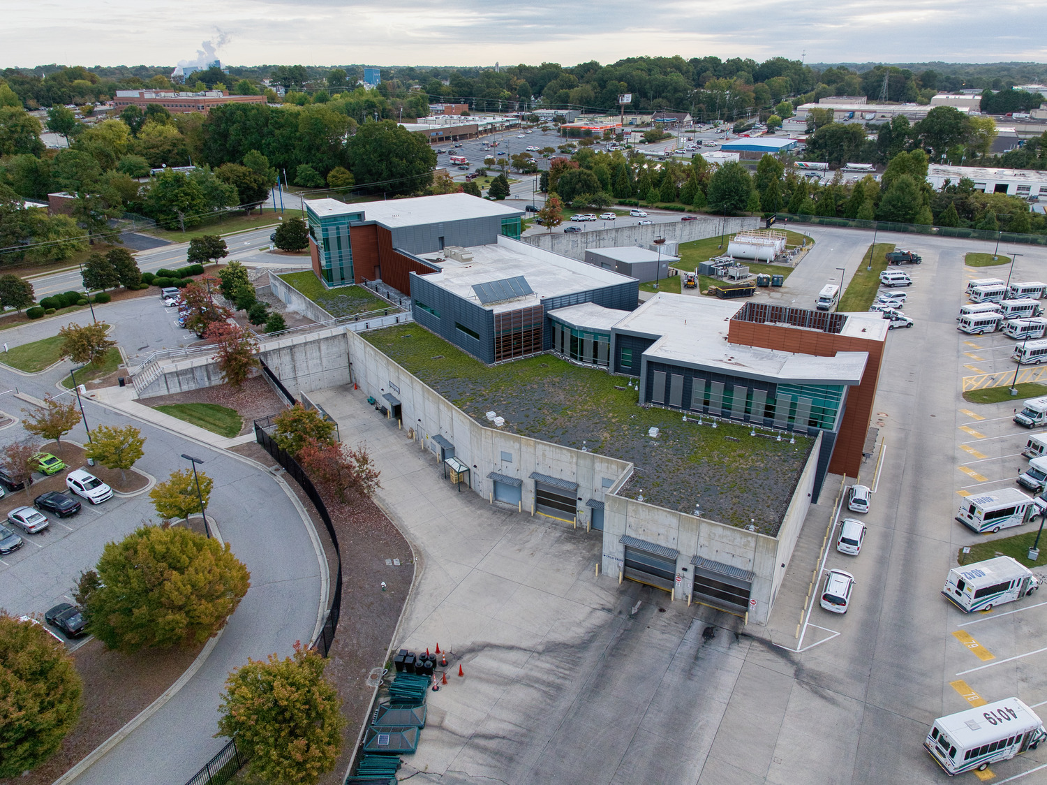 Behind the Greensboro Transit Authority building, rows of garages for fleet maintenance uphold the main headquarters. To the right, vehicles park in an open lot.