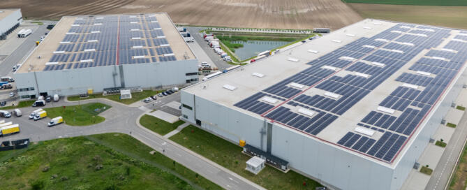 Aerial view of two industrial warehouses with solar panels on the roofs, part of a renewable energy microgrid system in a rural area.