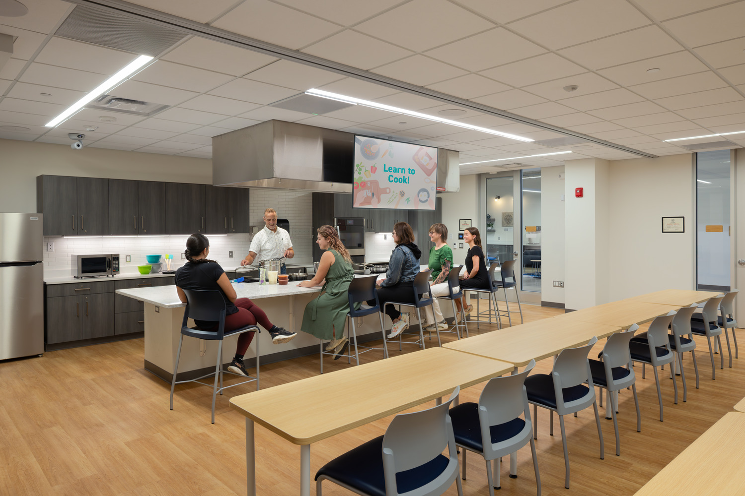 In a culinary classroom inside the GLOW YMCA, a group of students sit at a counter observing a cook.