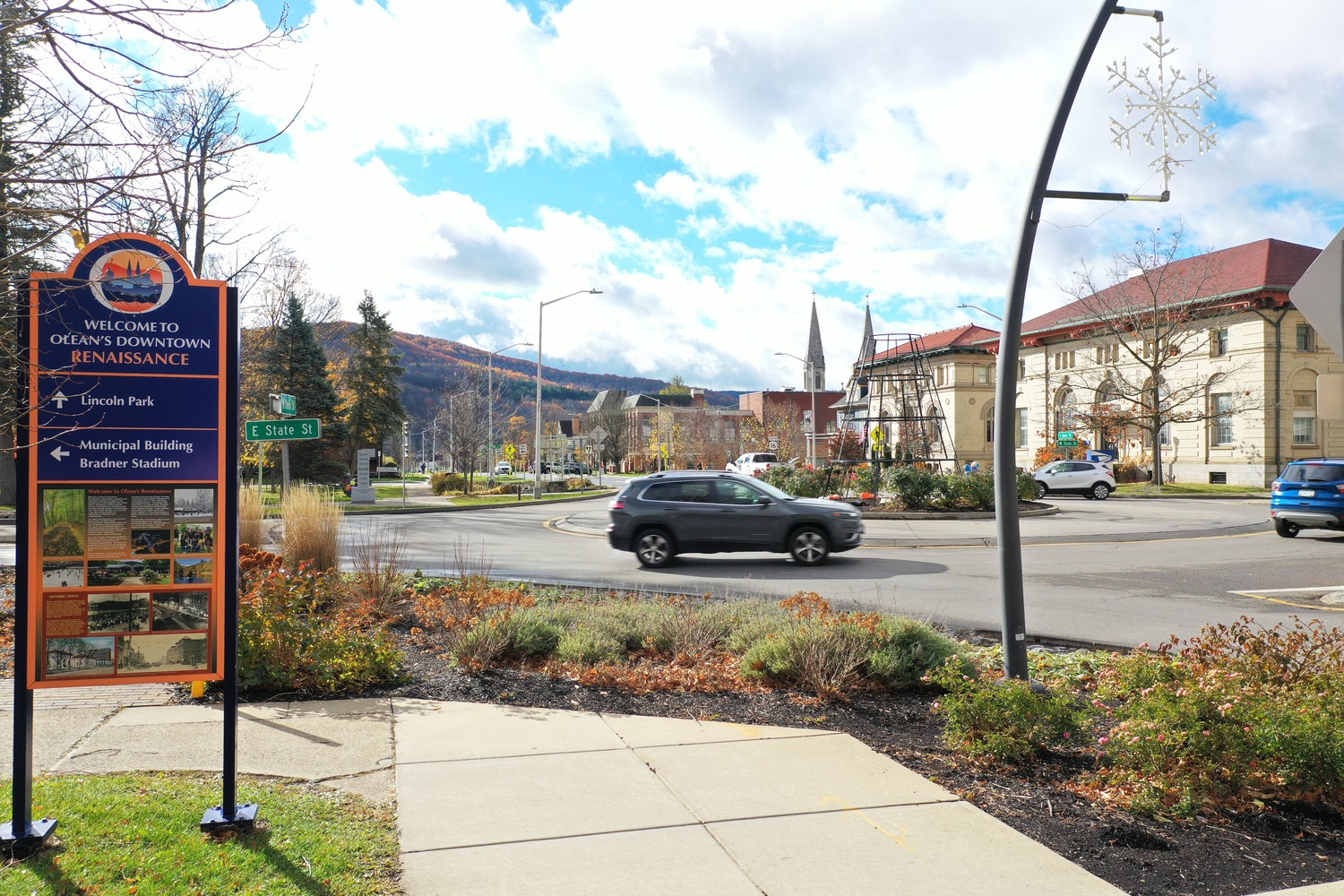 As part of the City of Olean South Union Streetscape revitalization, a sign next to a sidewalk says "Welcome to Olean's Downtown Renaissance" and points passerbys to various landmarks.
