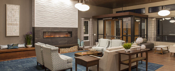 Senior-first design ROI reflected in a hospitality-inspired senior living lounge with ergonomic seating, layered lighting, acoustic carpet and warm materials.