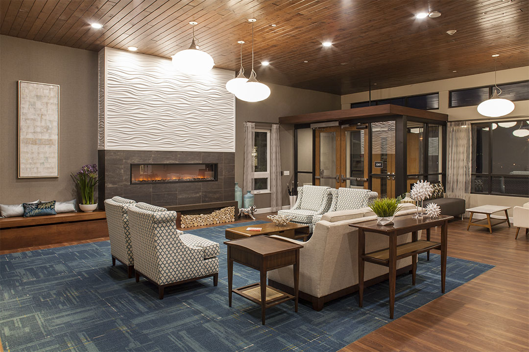 Senior-first design ROI reflected in a hospitality-inspired senior living lounge with ergonomic seating, layered lighting, acoustic carpet and warm materials.