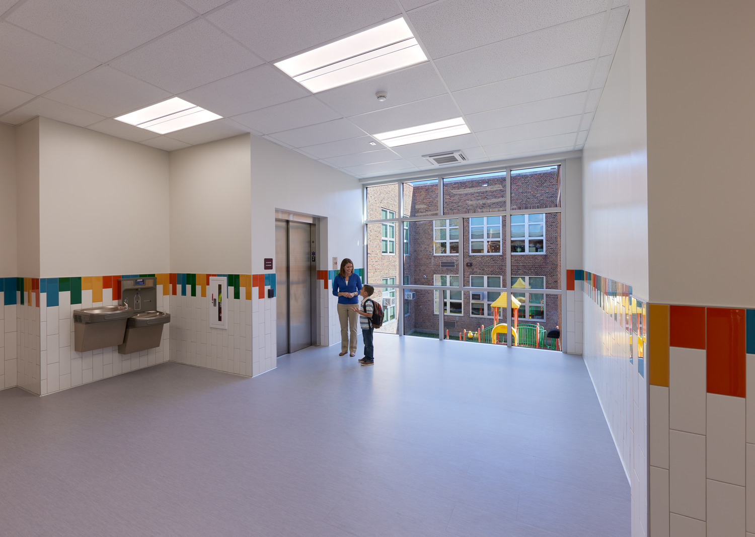 An elevator entrance and floor-to-ceiling windows overlooking a playground at Ossining UFSD Park Elementary School.