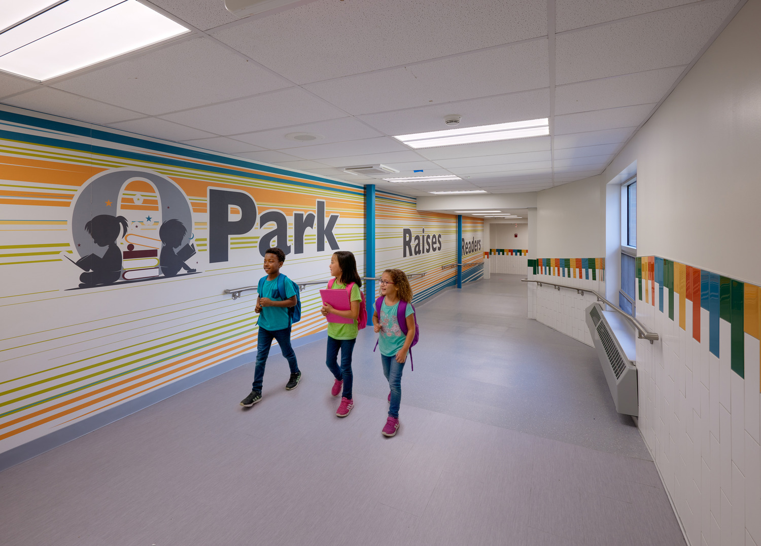 Three kids walk through a colorfully painted Ossining UFSD Park Elementary School hallway.