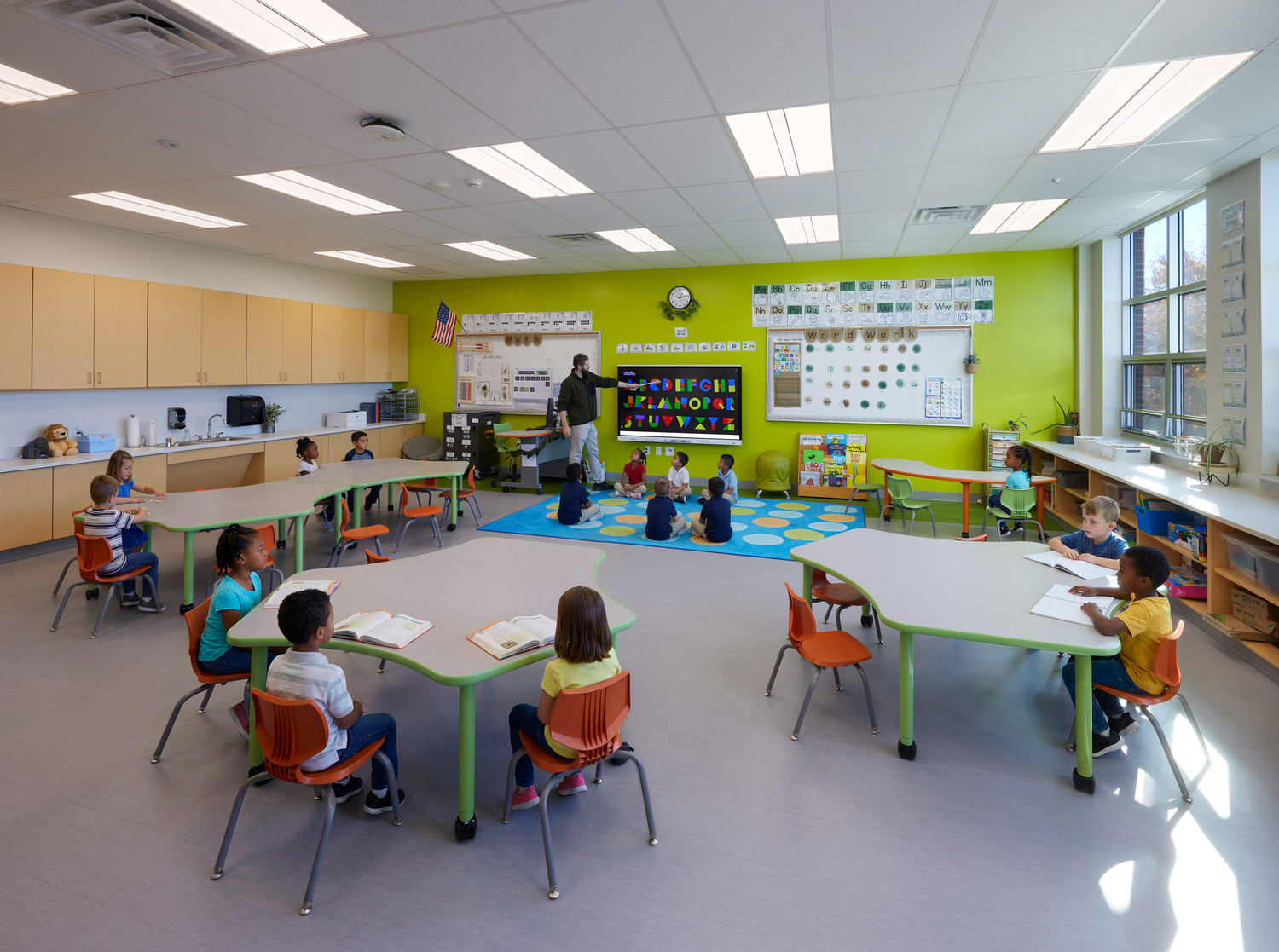 A teacher points to the board at the front of a spacious classroom at Ossining UFSD Park Elementary School with a lime green accent wall and colorful decorations.