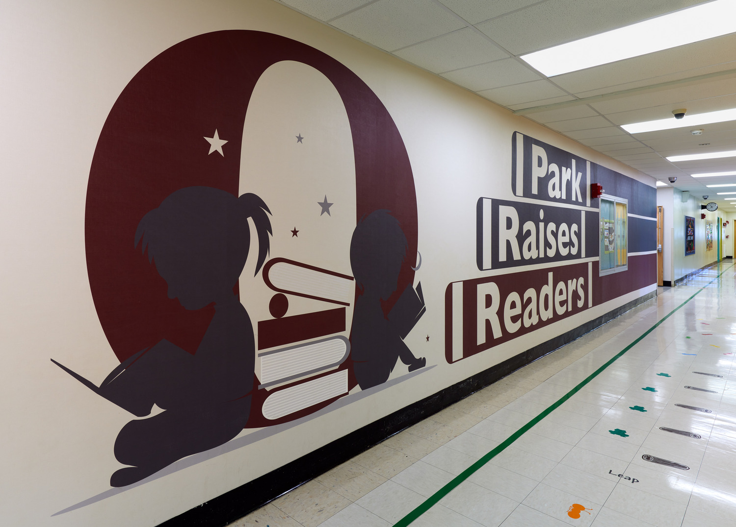 A hallway in Ossining UFSD Park Elementary School has maroon wall art of silhouetted kids reading, with the words "Park Raises Readers".