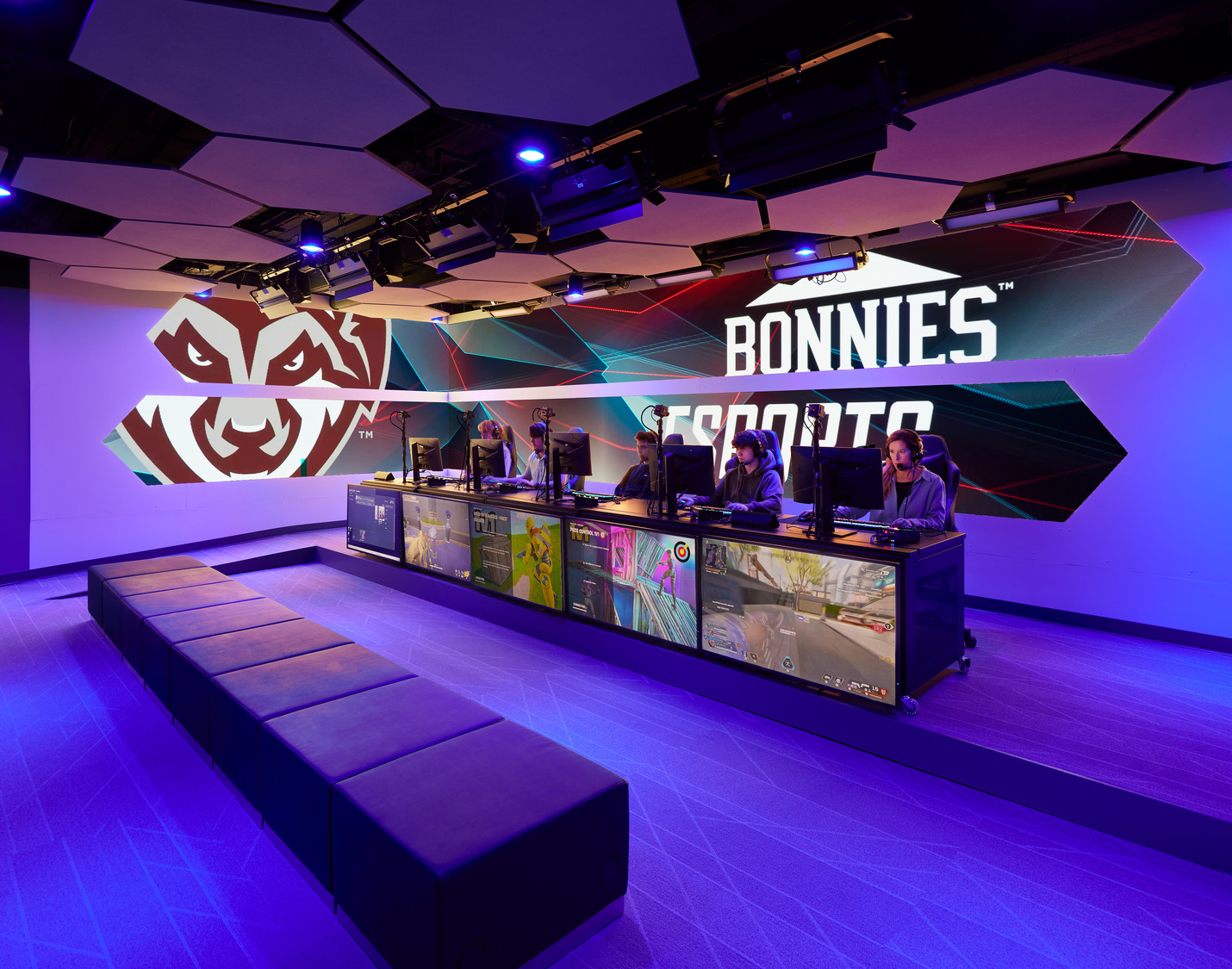 Completed competitive esports arena at St. Bonaventure University featuring a dedicated team competition stage, professional PC gaming stations, integrated broadcast displays, acoustic ceiling panels, and branded graphic walls with dynamic lighting.