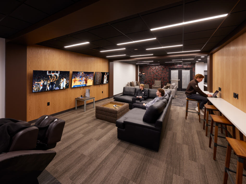 In the renovated Men's Basketball Locker Room at St. Bonaventure, a group of athletes sit in a common area watching TV or studying.,
