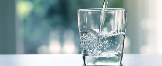 Water being poured into a clear glass, which sits atop a gray counter.