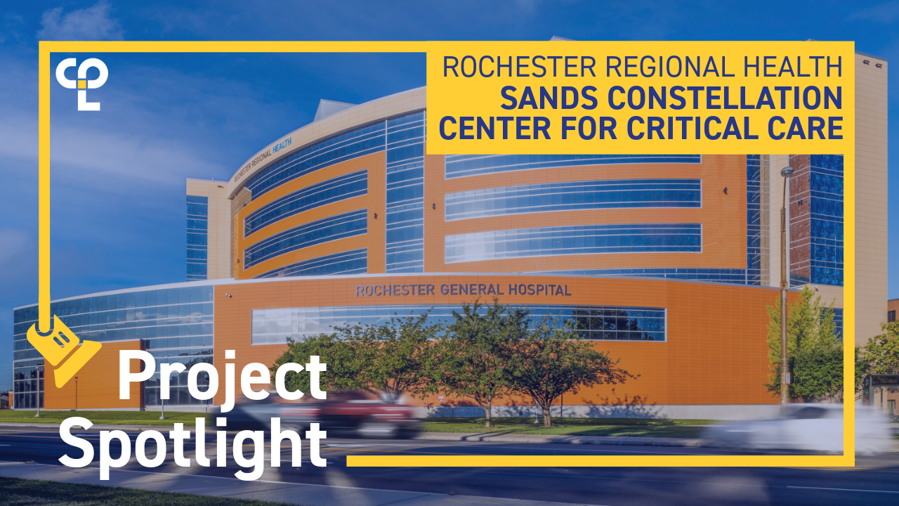 Alt text: "A modern hospital building with a curved facade under a blue sky, labeled 'Rochester General Hospital'. Foreground text reads 'Project Spotlight', 'Rochester Regional Health', and 'Sands Constellation Center for Critical Care', with a graphic of a spotlight and the CPL logo. Vegetation and a moving car are visible in front."
