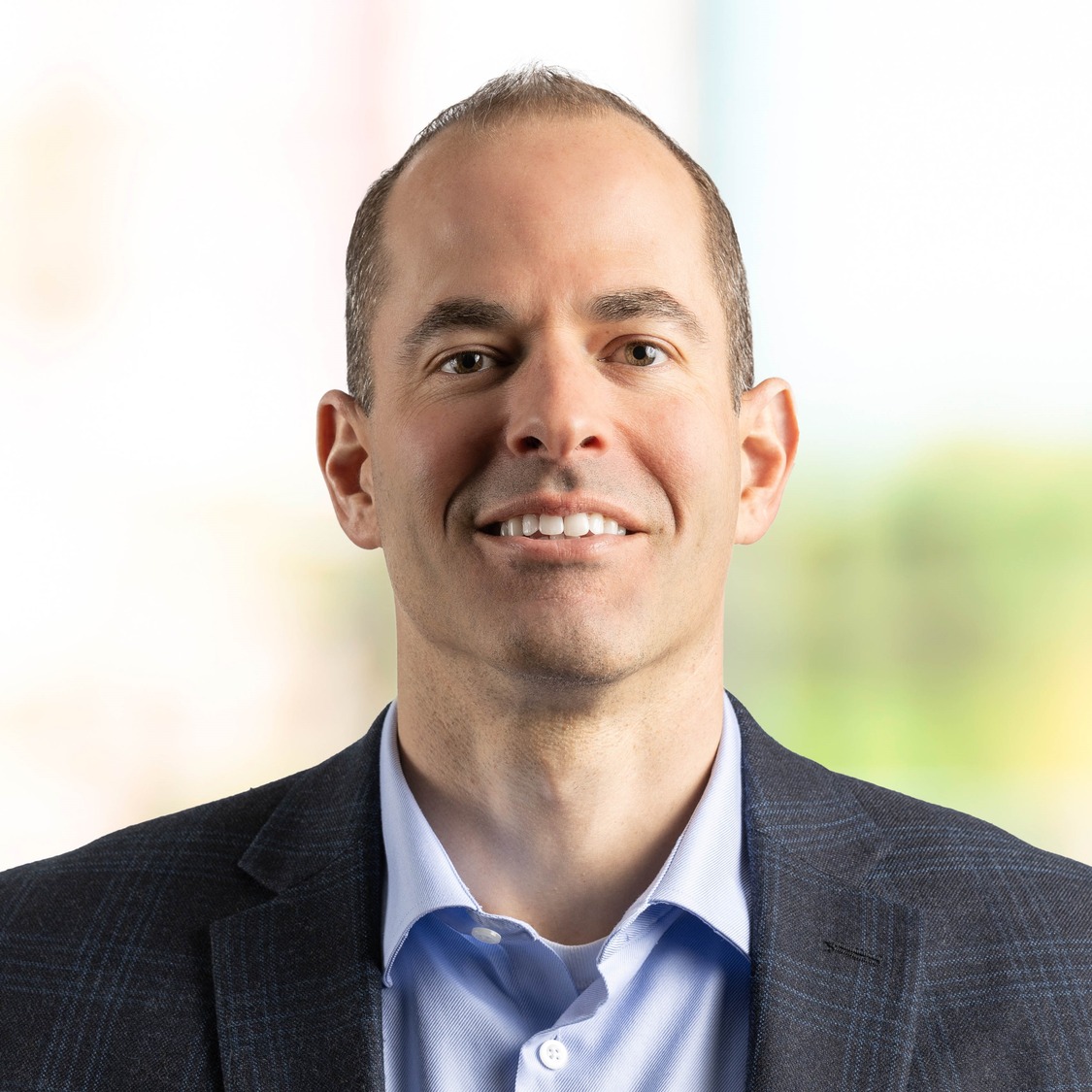 Man in blue shirt and navy jacket smiling on green background