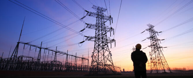Electricity worker silhouette observes energy infrastructure outside.