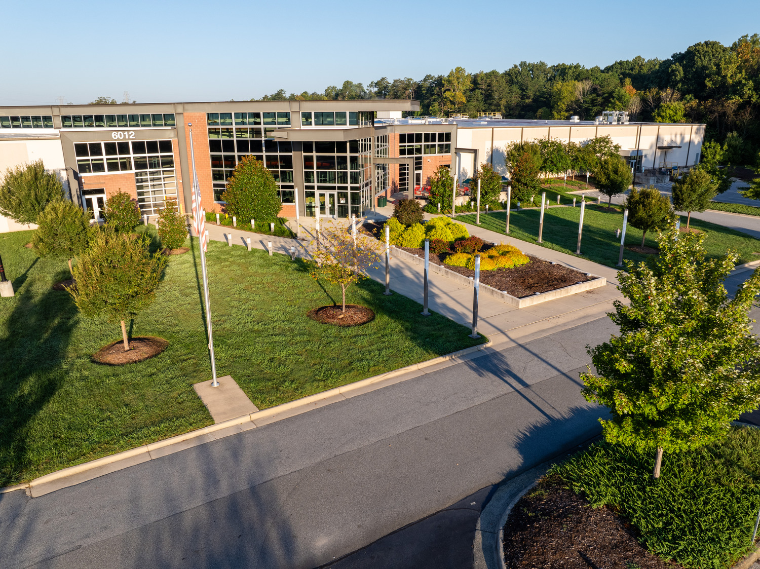 R17_50048_00_GTCC_N3_medium Modern building with large glass windows and a red brick facade. A landscaped garden with vibrant green shrubs lines the entrance pathway under clear blue skies at GTCC.