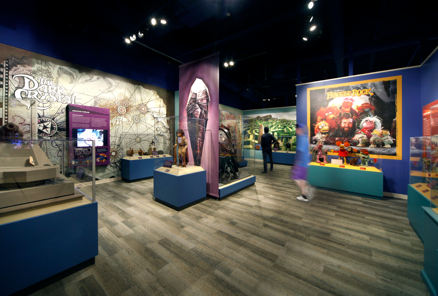 12882_00_Center_for_Puppetry_Arts_N45_HumanityEdit1 A museum exhibit in the Center of Puppetry Arts with fantasy and puppet themes, featuring displays from "The Dark Crystal" and "Fraggle Rock." Visitors explore colorful showcases.