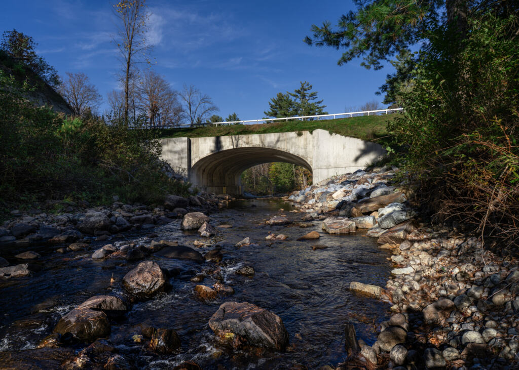 Culvert and bridge over a river and small waterfall in Warren County on a bright sunny day.