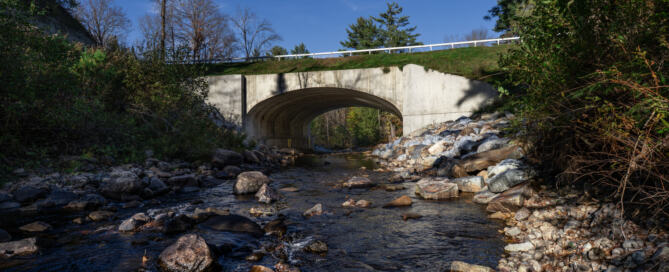 Culvert and bridge over a river and small waterfall in Warren County on a bright sunny day.