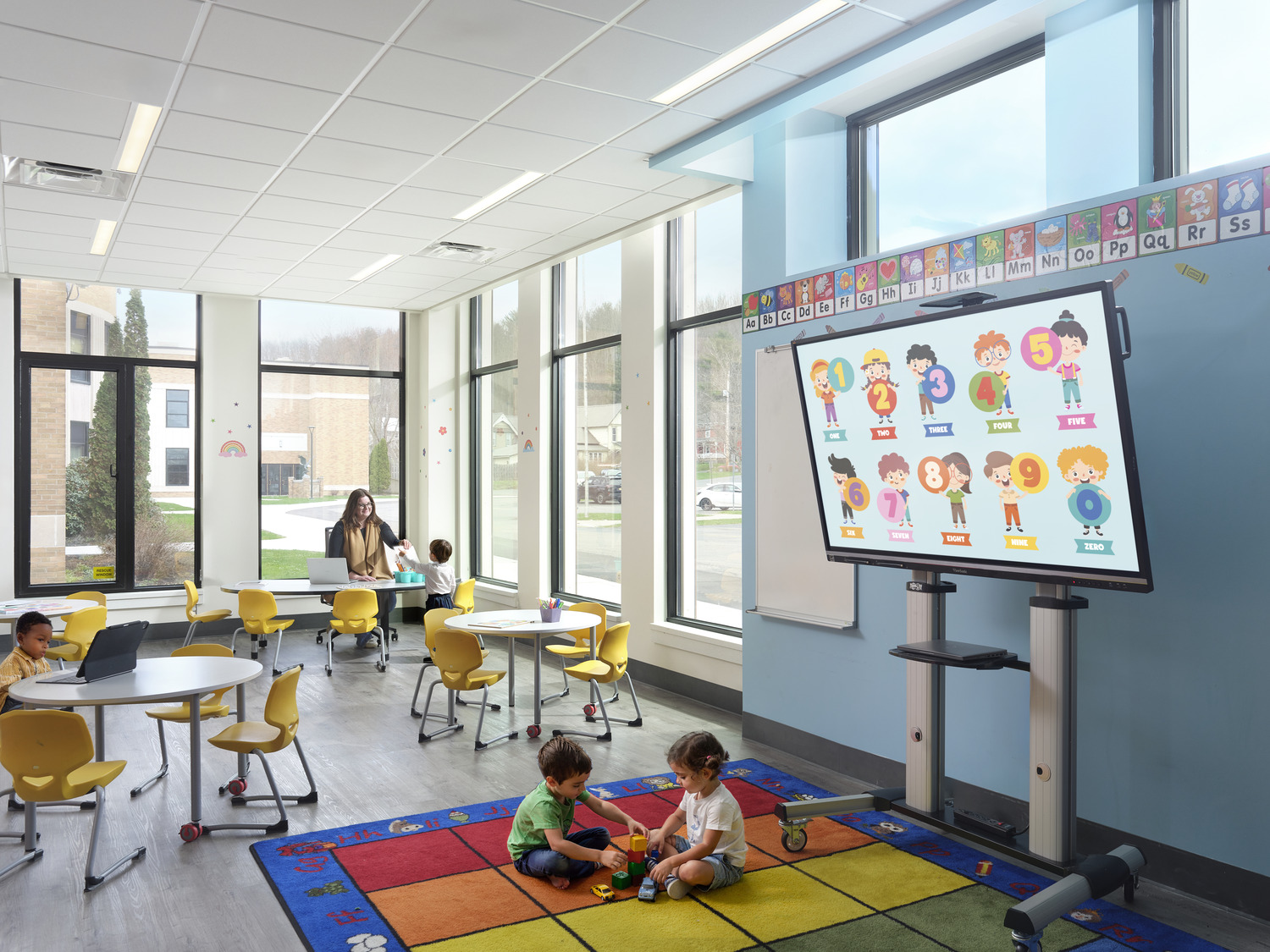 Young students sit and play on a colorful rug in a brightly illuminated preschool classroom, part of Fillmore's Capital Improvement project.