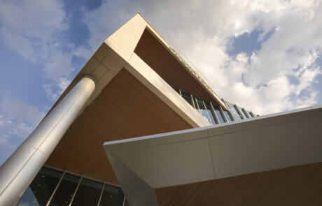 A modern building viewed from a low angle against a blue sky with clouds. It features glass and wood accents, creating a sleek and contemporary look.