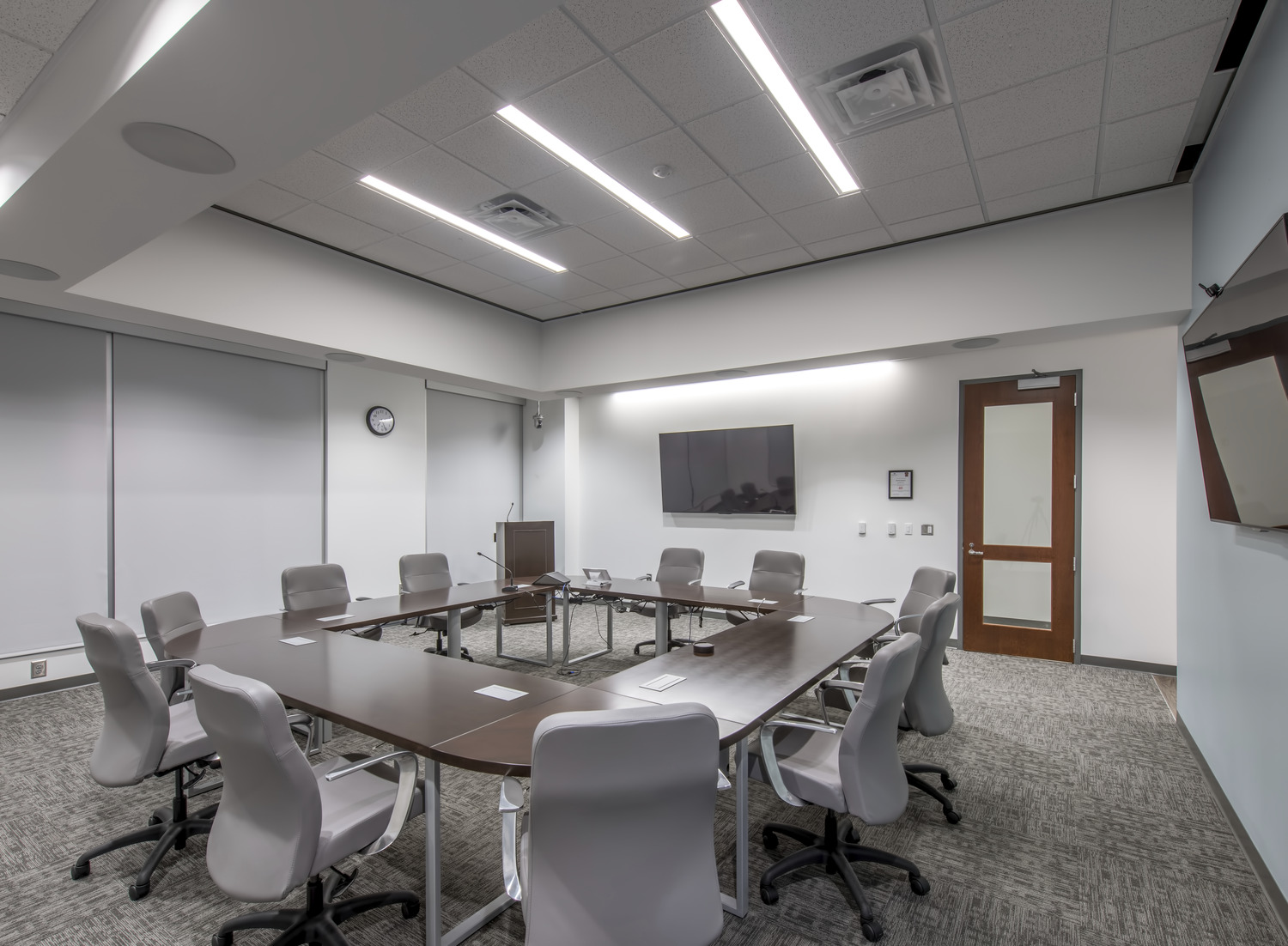 Modern conference room with leather chairs around a square conference table with monitors mounted on the walls and a podium at the Johns Creek Municipal Center