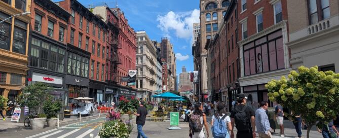 A group of people walk down a busy street on a sunny day.